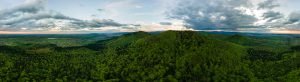 Aerial wide panoramic view of dark mountain hills covered with green mixed pine and lush forest in evening
